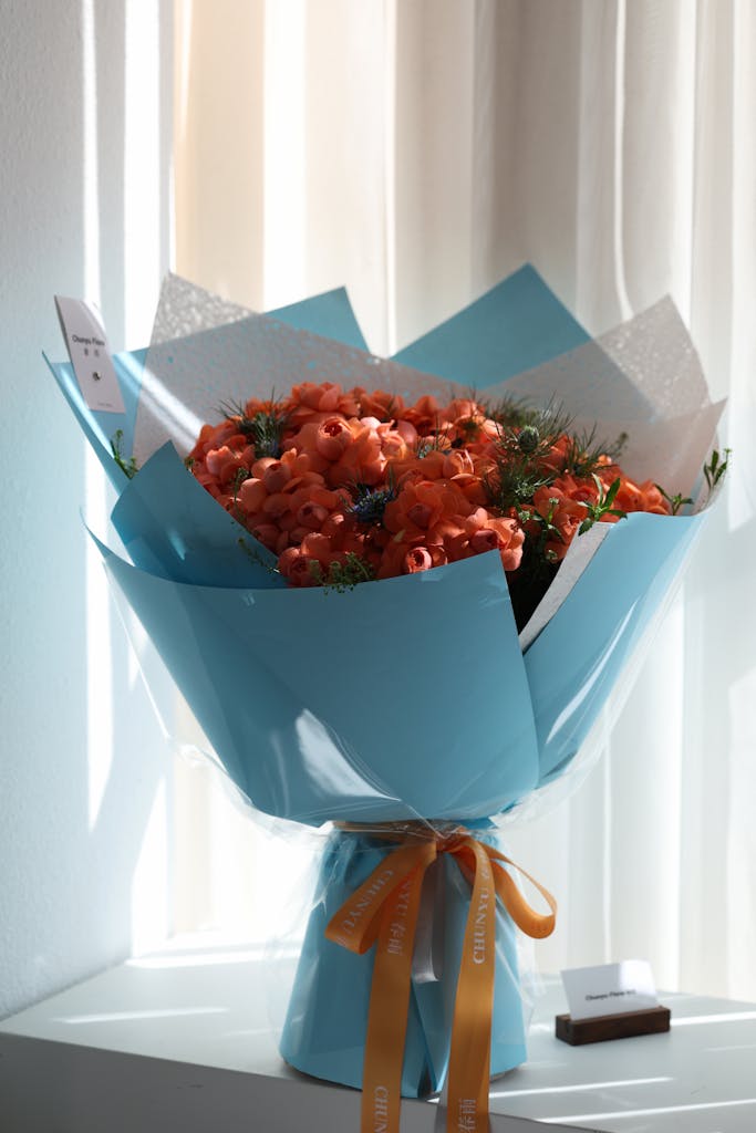 A beautiful bouquet of orange flowers wrapped in blue paper, perfect for gifting.